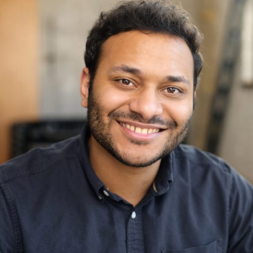 Cheerful and serene hindu man in smart casual shirt, headshot of young handsome indian guy, handsome mixed-race male looks at the camera with toothy smile